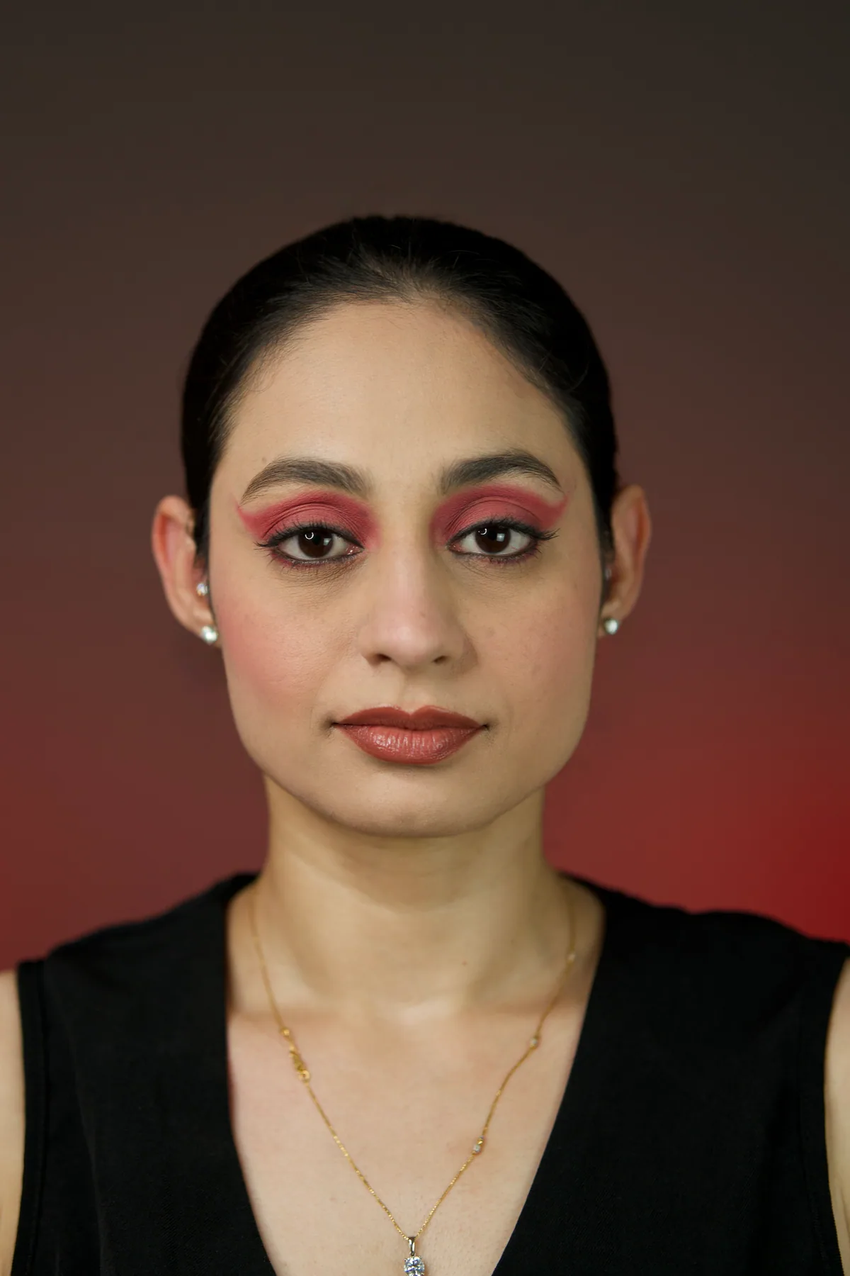 Editorial self makeup portrait on Gurvani with crimson winged eye makeup, soft sculpted skin, and a warm studio backdrop